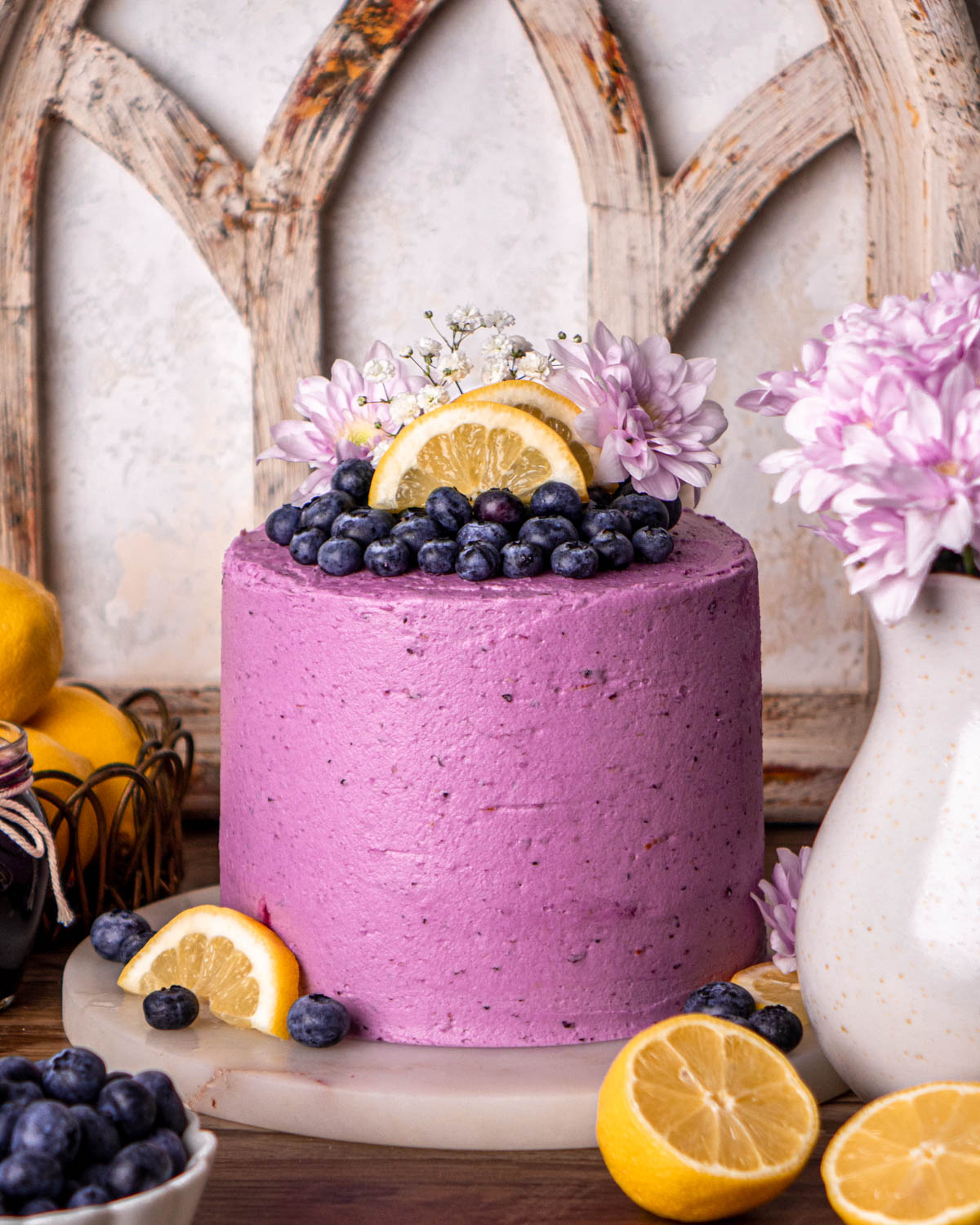 blueberry lemon cake frosted with purple frosting, topped with blueberries, lemon slices and flowers