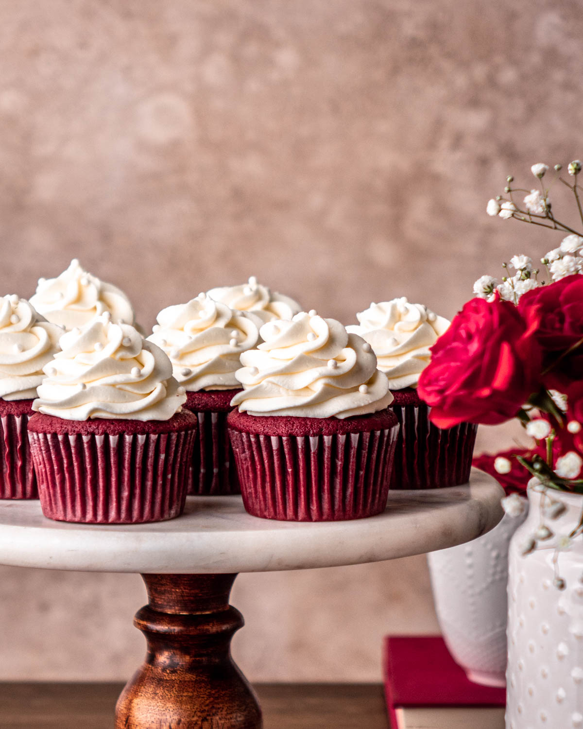 red velvet cupcakes on a cake stand with red roses in front