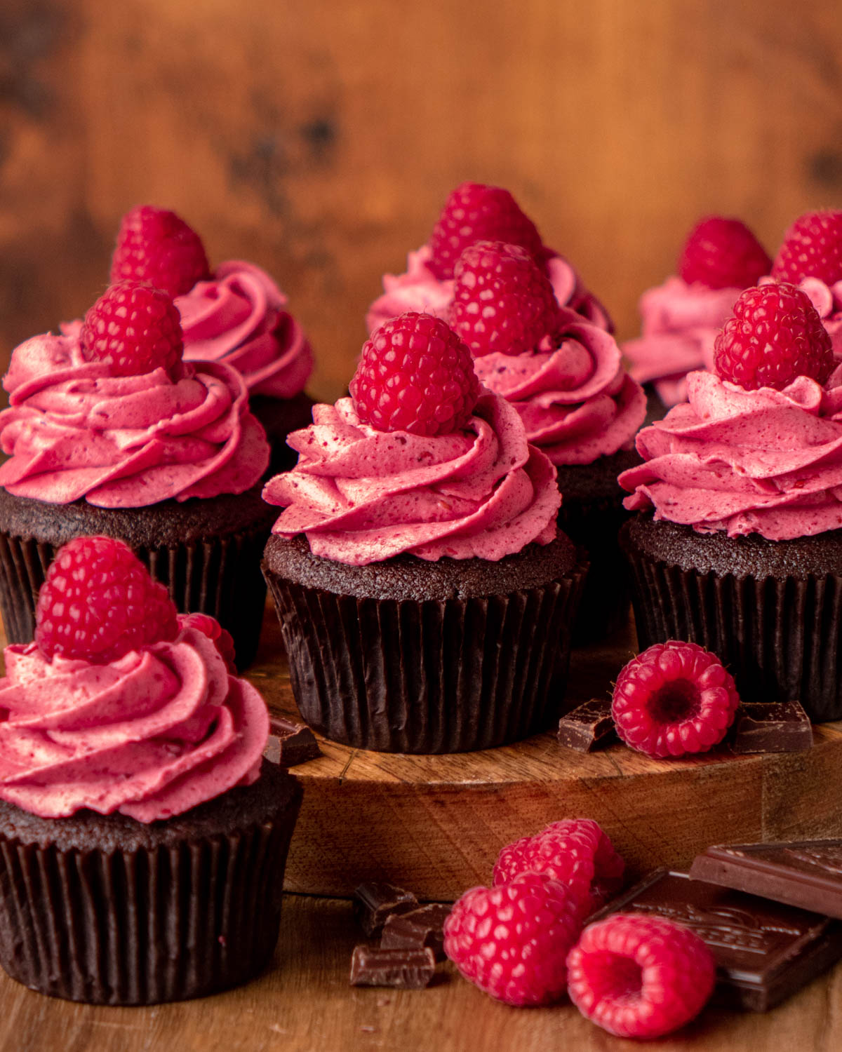 chocolate raspberry cupcakes on a wood platter with raspberries and chocolate around