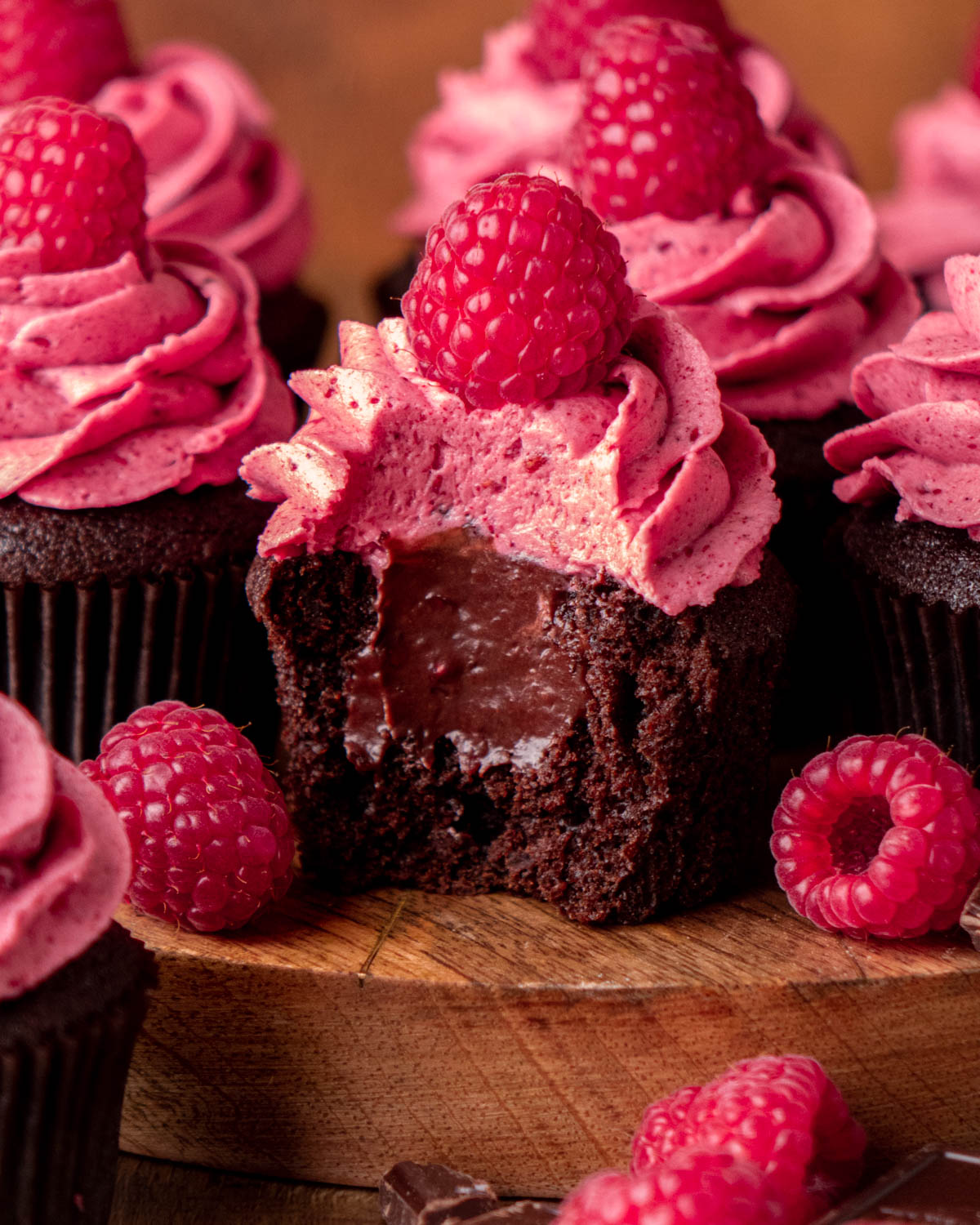 a chocolate raspberry cupcake with a bite taken out to reveal a ganache center with other cupcakes around