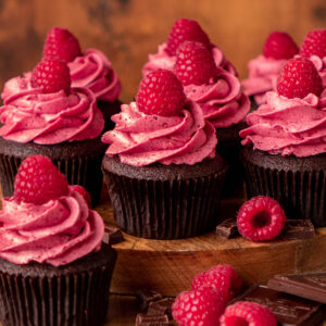 chocolate raspberry cupcakes on a wood platter with raspberries and chocolate around