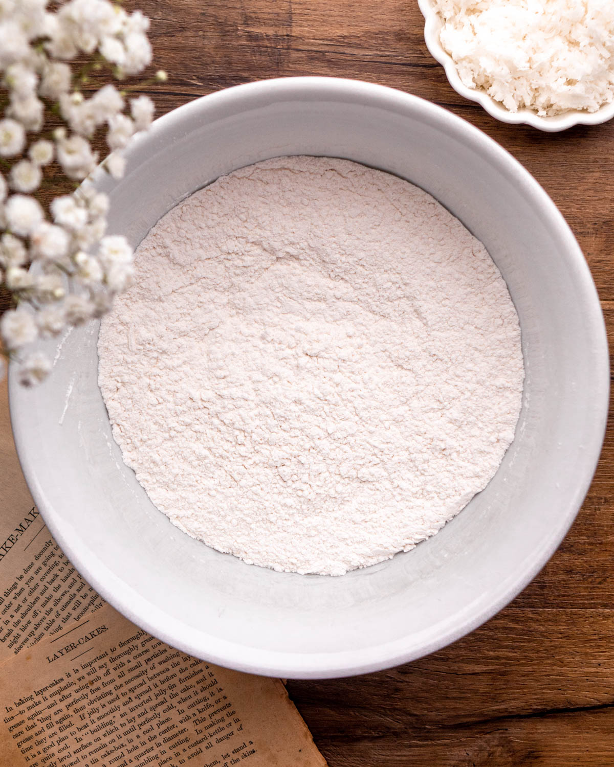 cake flour, baking powder, baking soda and salt whisked together in a white bowl on a wood board 