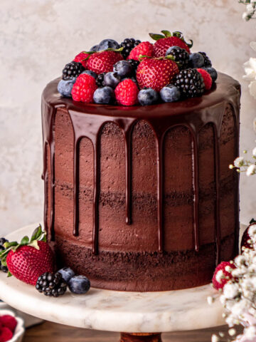chocolate cake with chocolate ganache drip topped with strawberries, blueberries, raspberries and blackberries.