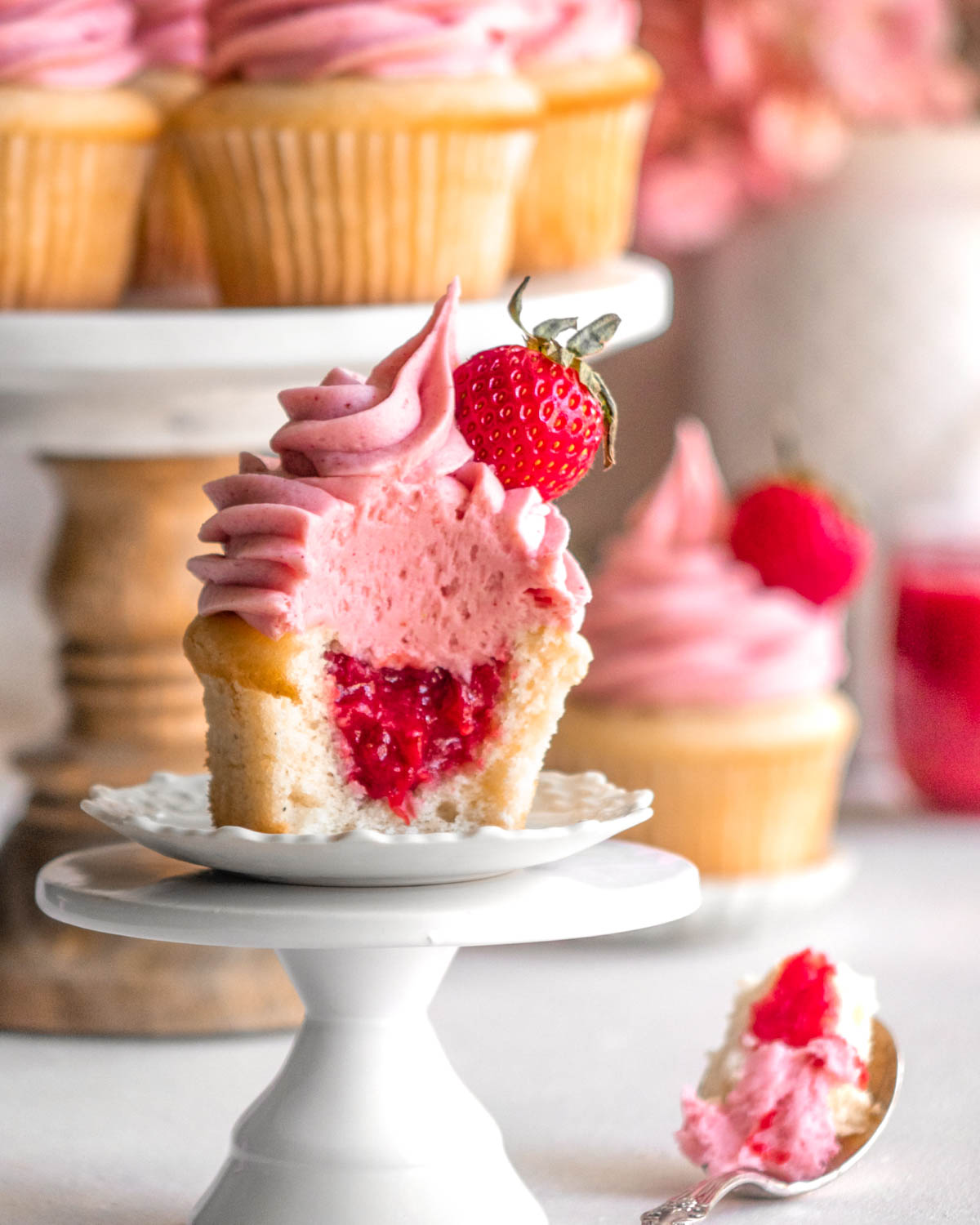 strawberry cupcake on a cupcake holder with a bite taken out, with other cupcakes in the background 