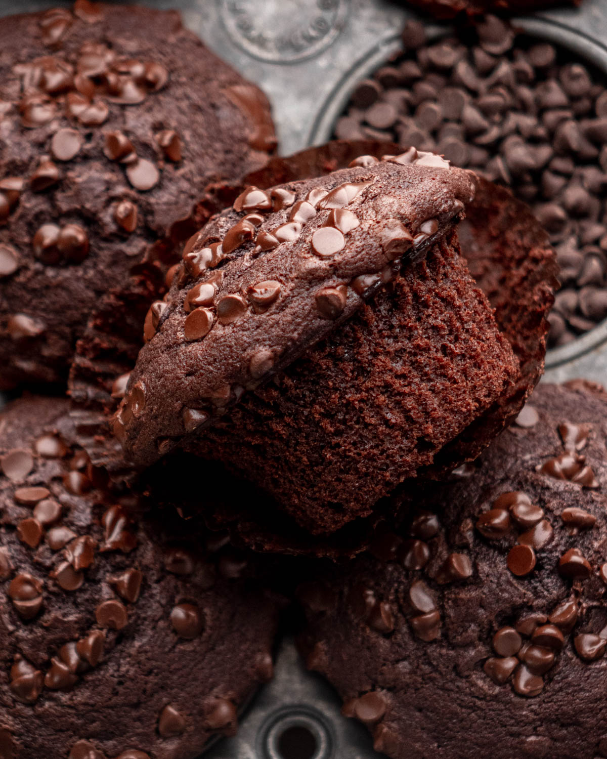 close up of chocolate muffin laying on other chocolate muffins with wrapper taken off