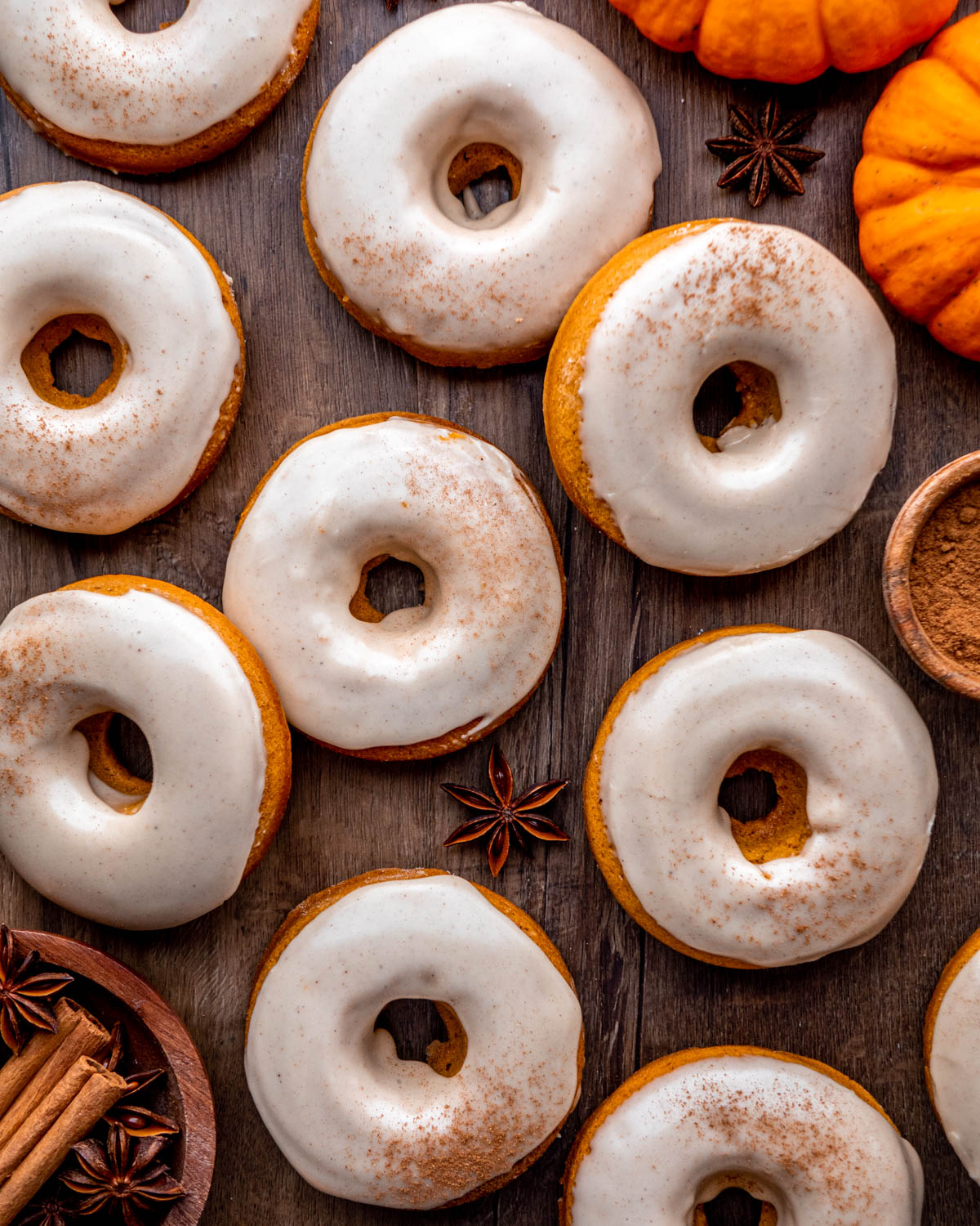 pumpkin donuts on a wood board with pumpkins, cinnamon sticks and star anise around