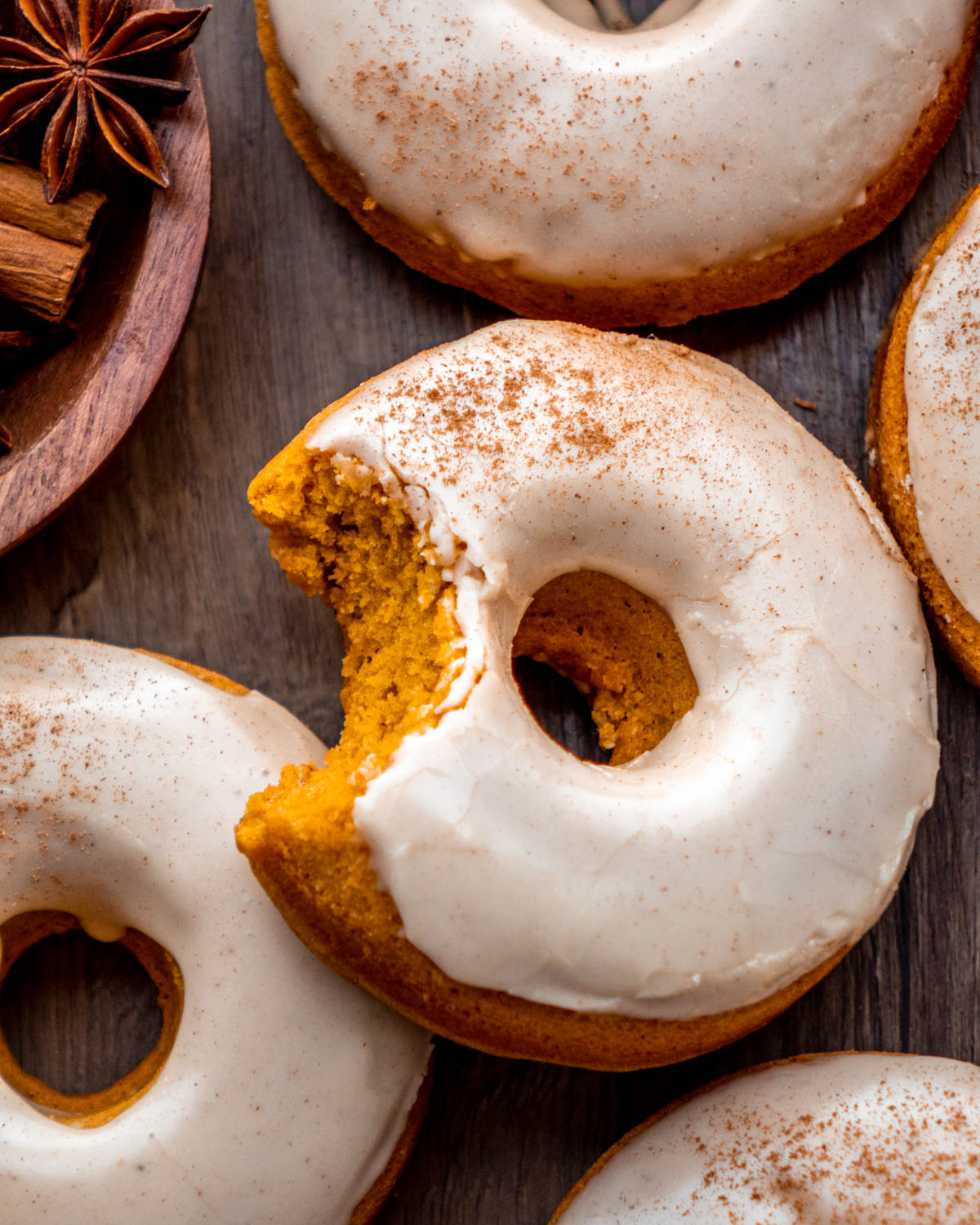 pumpkin donuts with a bite taken out on a wood board 