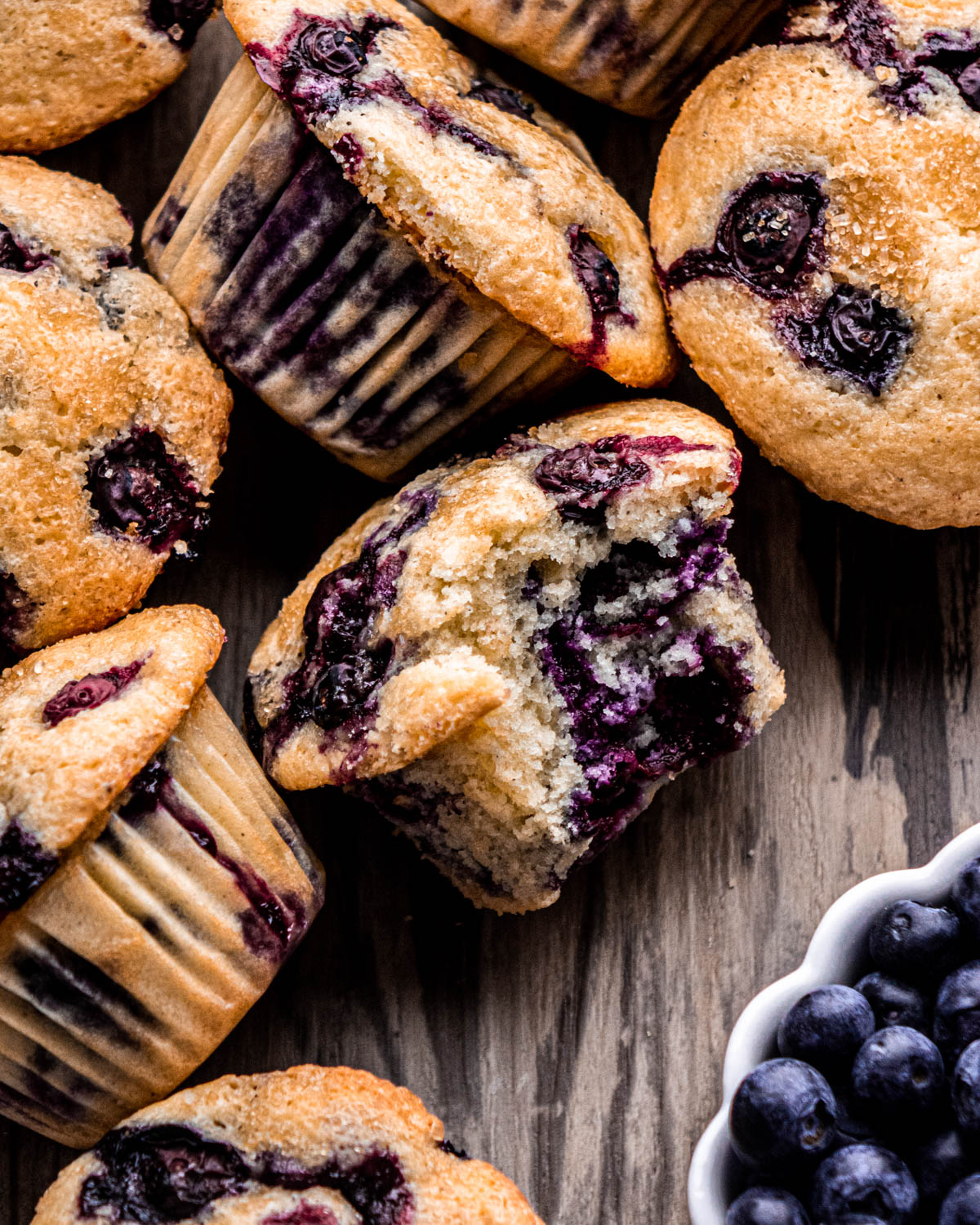 close up of blueberry muffins on wood board, one with bite taken out