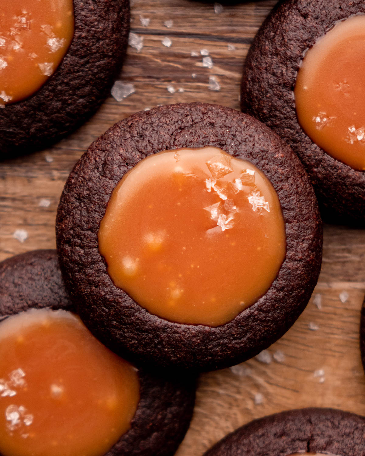 close up of a chocolate caramel cookie on top of other cookies on a wood board