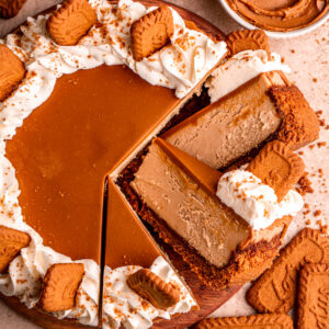 biscoff cheesecake cut into slices arranged on each other on a wood board decorated with whipped cream and Biscoff cookies