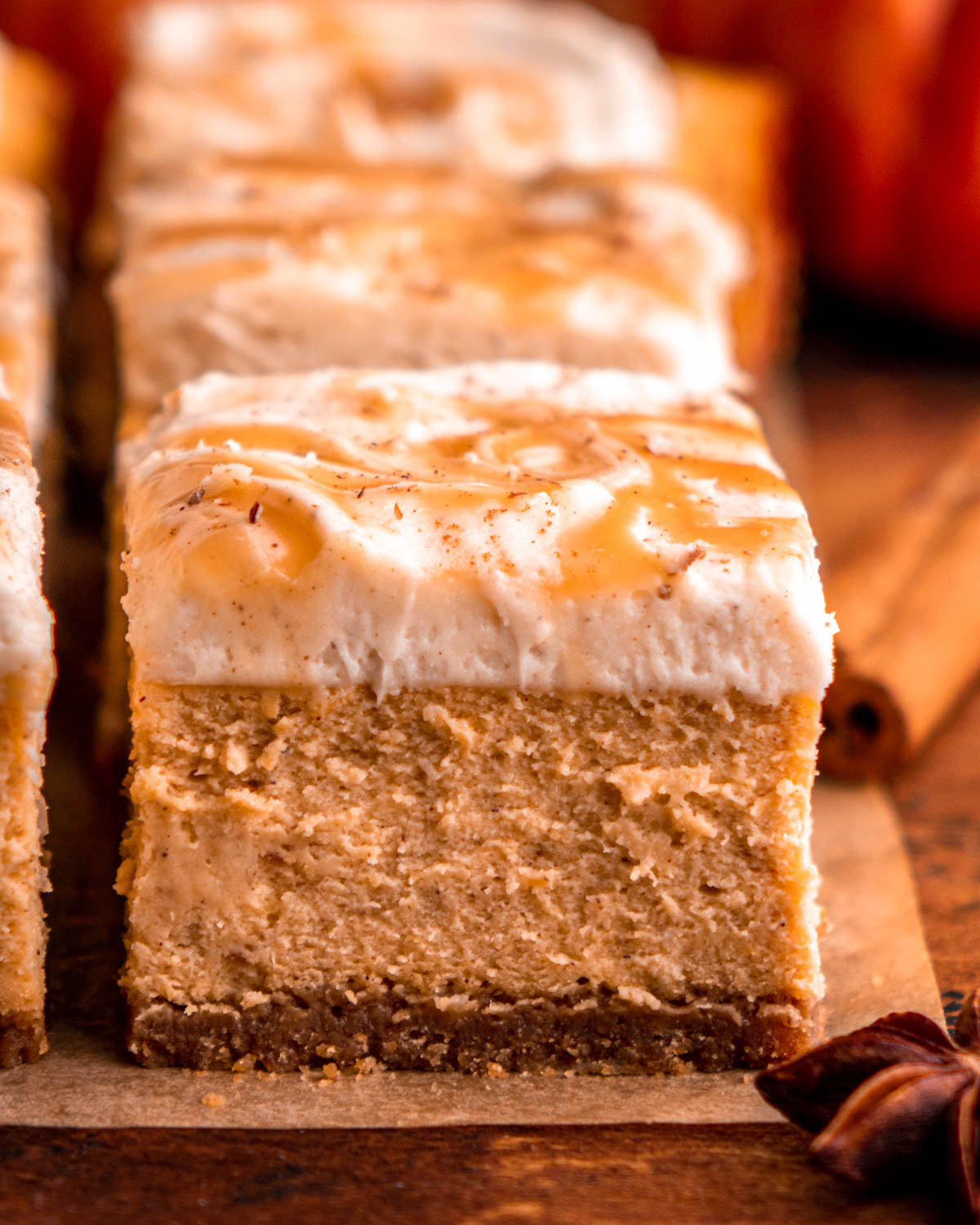close up of a pumpkin cheesecake bar topped with cream cheese frosting and caramel sauce