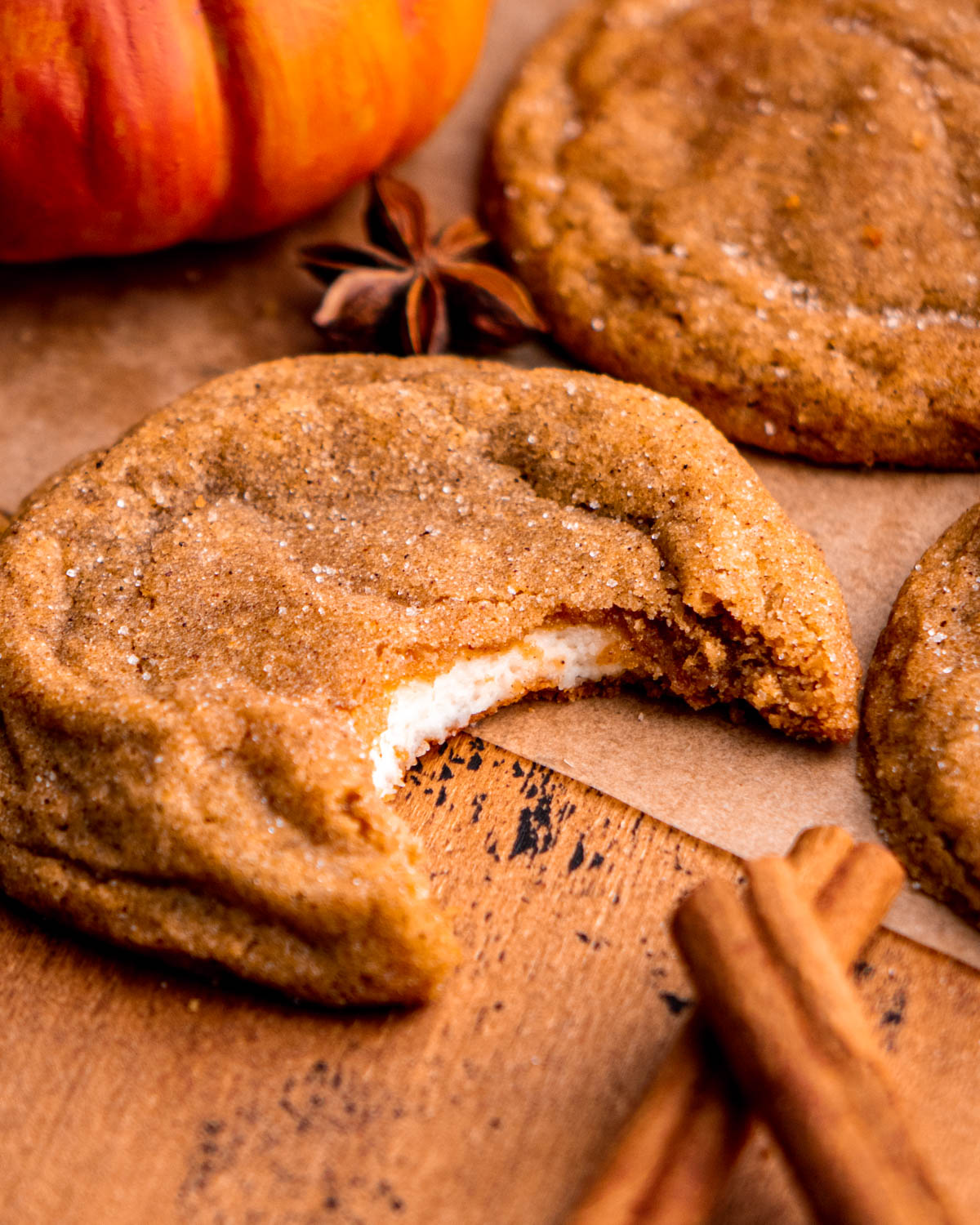 pumpkin cheesecake cookie with a bite taken out with other cookies, cinnamon sticks, star anise and pumpkins around