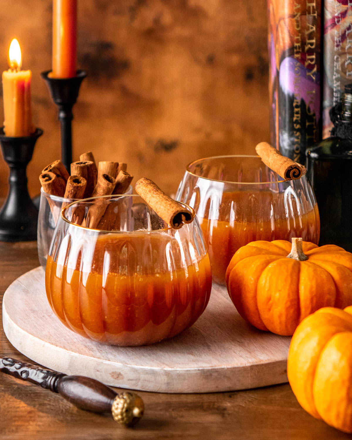 two glasses of pumpkin juice on a wood board with pumpkins, candles and books around
