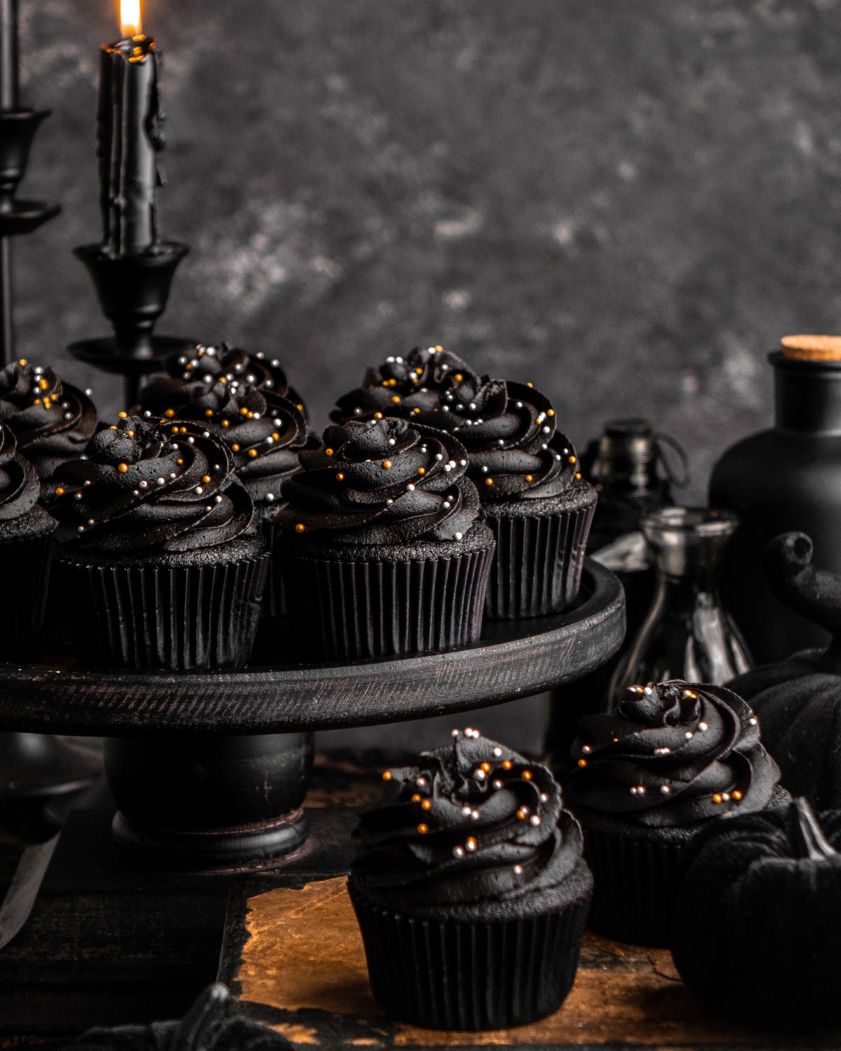 black velvet cupcakes on a black cake stand with black candles and bottles in background 