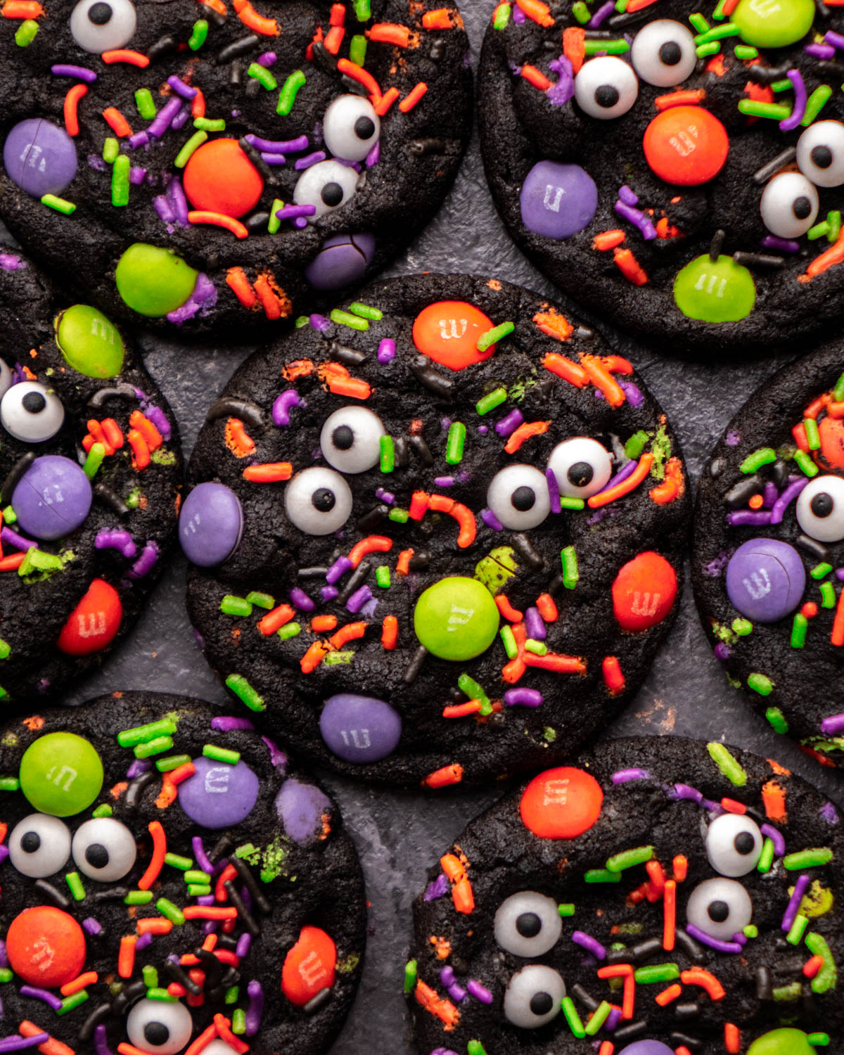 black halloween cookies covered in halloween sprinkles, M&Ms and candy eyeballs arranged around each other