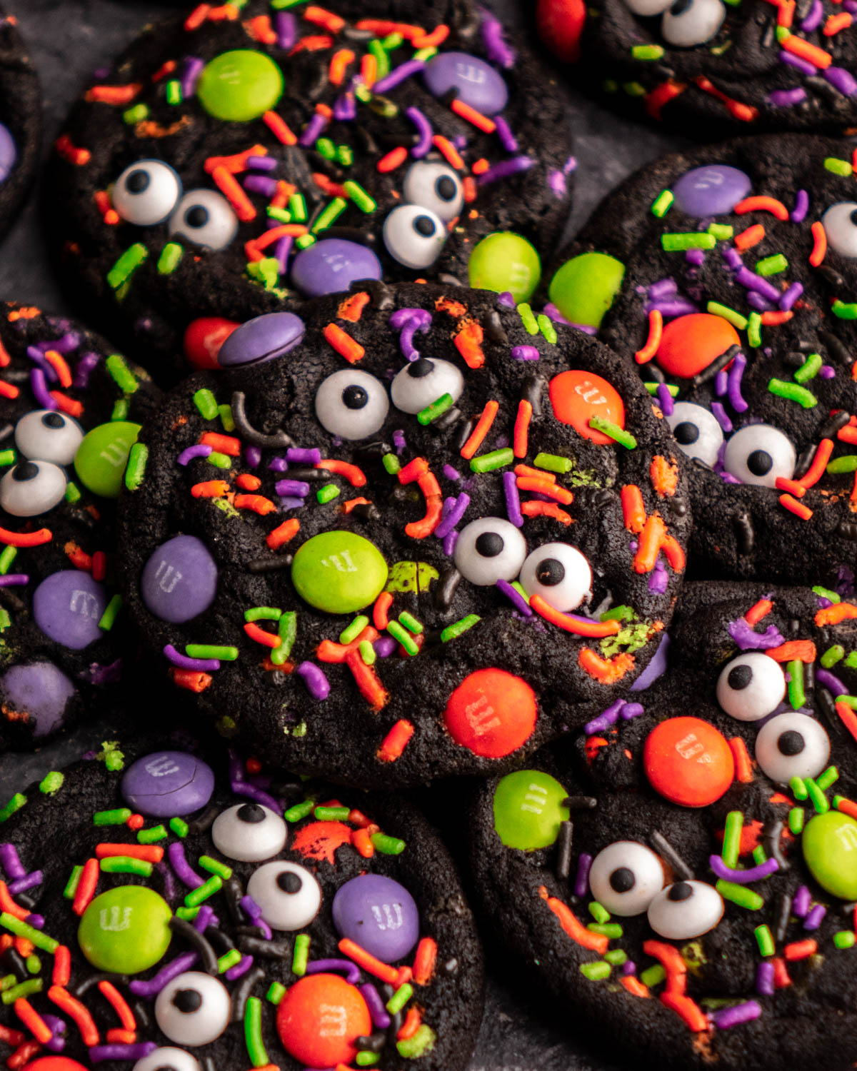 black halloween cookie covered in halloween sprinkles, M&Ms and candy eyeballs