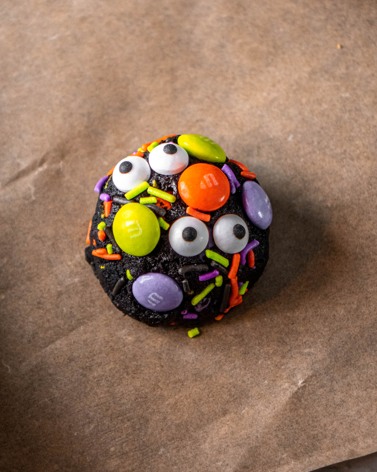 close up of dough scooped into a ball and covered in Halloween M&Ms, sprinkles and candy eyeballs