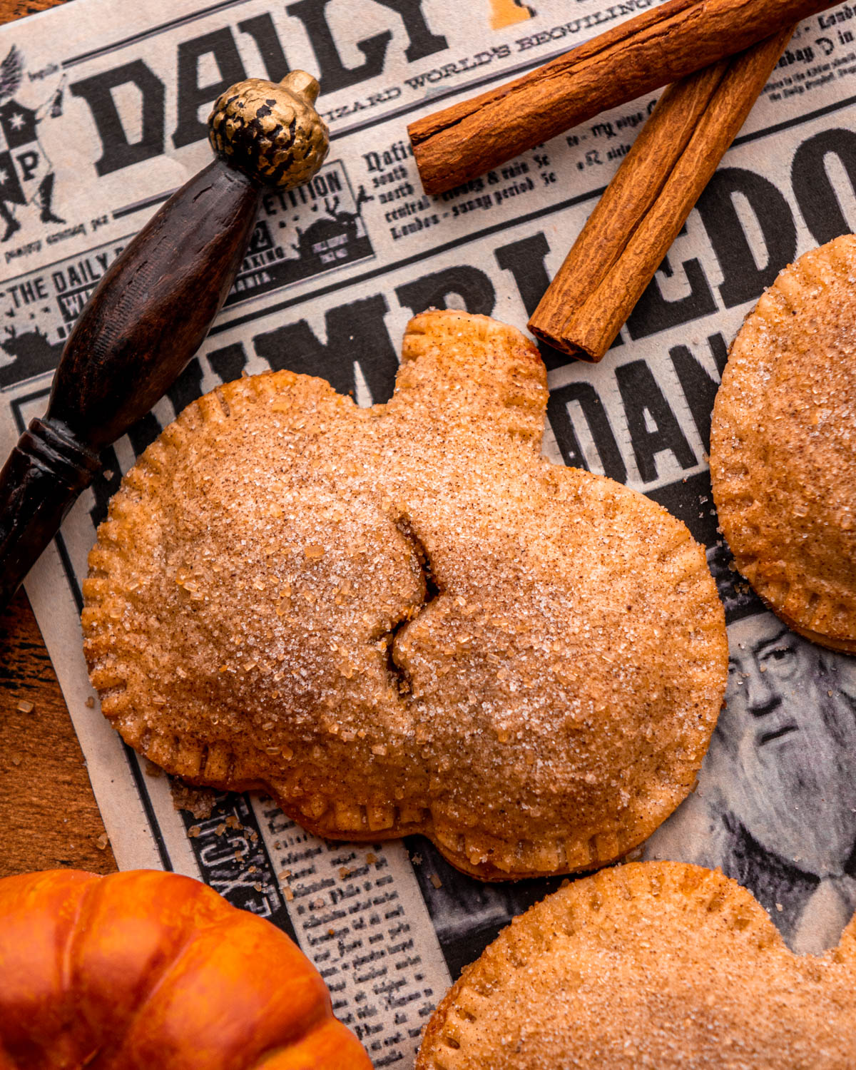 close up of a pumpkin pasty on newspaper with pumpkins, a wand and cinnamon sticks around