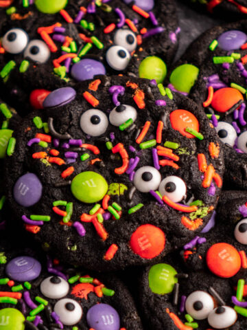 black halloween cookie covered in halloween sprinkles, M&Ms and candy eyeballs