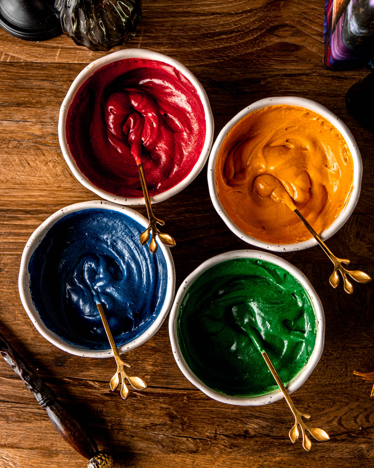 cream cheese frosting in four bowls, dyed red, gold, green and blue