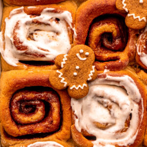 close up of four gingerbread eggnog cinnamon rolls with a mini gingerbread cookie