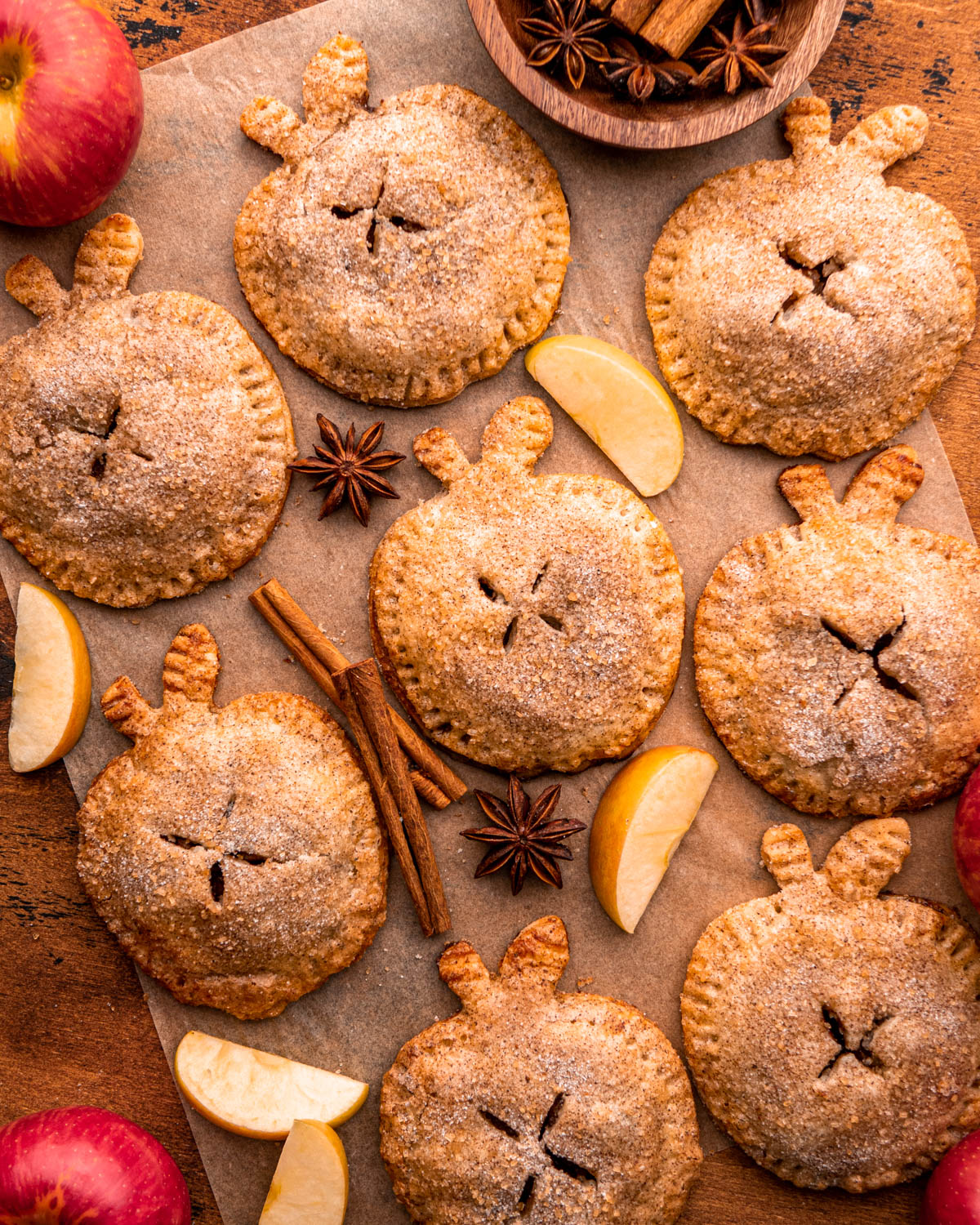 mini apple pies arranged on parchment paper with apples, star anise and cinnamon sticks around 