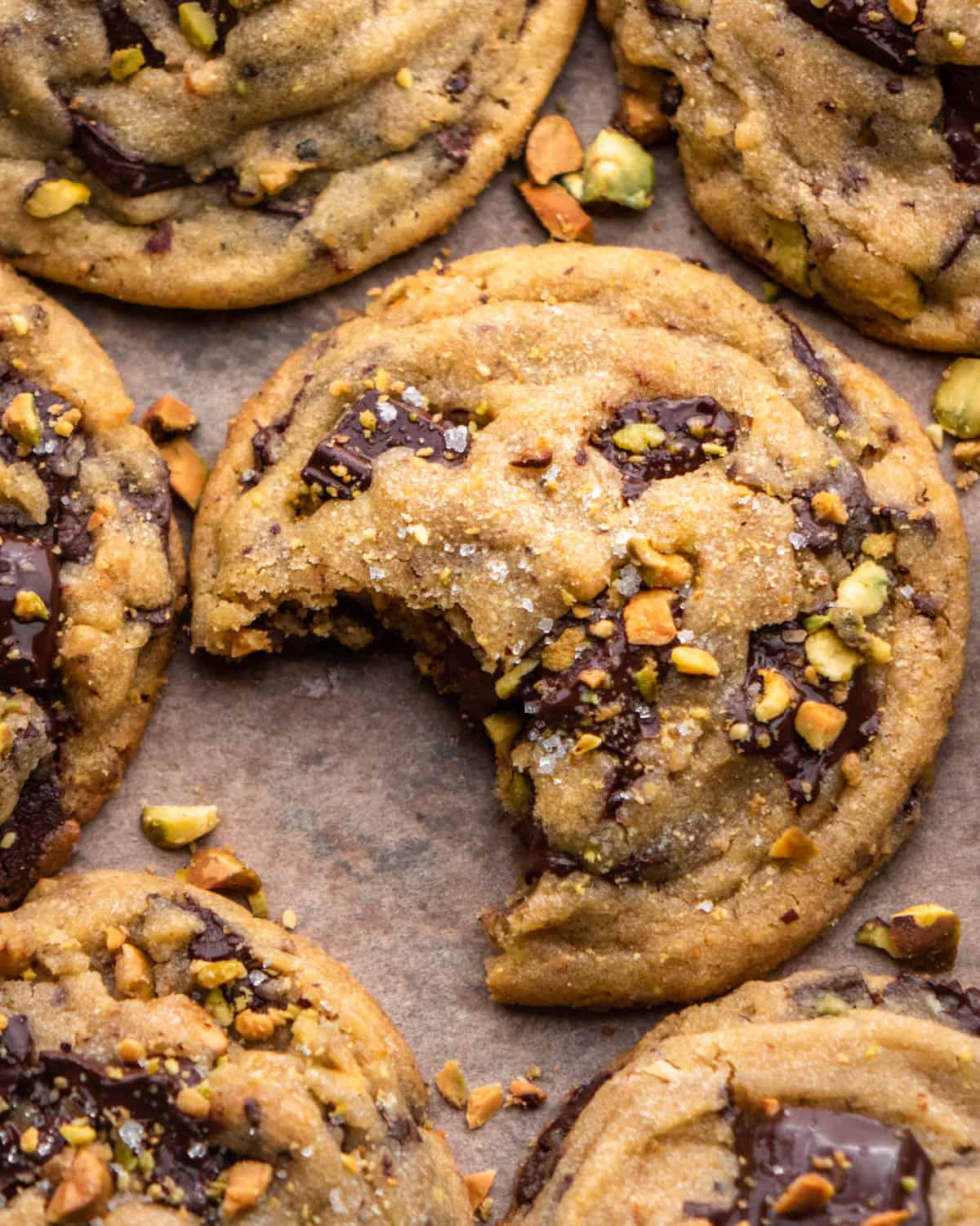 pistachio cookie with bite taken out on parchment paper with other cookies around