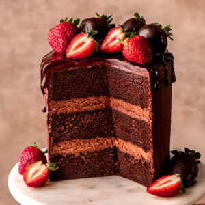 chocolate ganache cake sliced open with strawberries on top on a marble cake stand