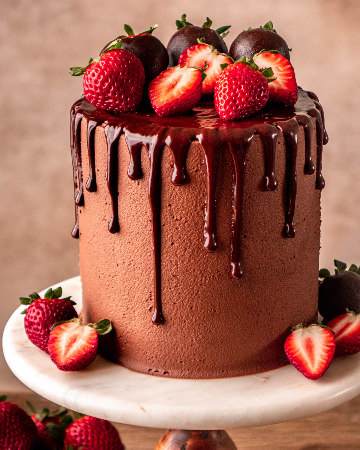 chocolate ganache cake decorated with a chocolate drip and strawberries on a marble cake stand 