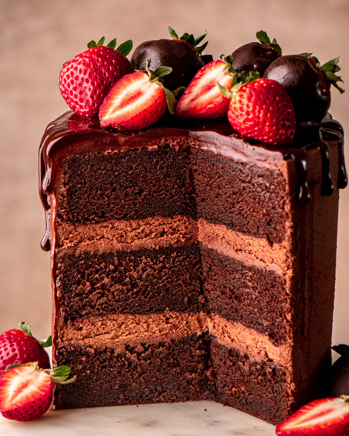 chocolate ganache cake sliced open with strawberries on top on a marble cake stand 
