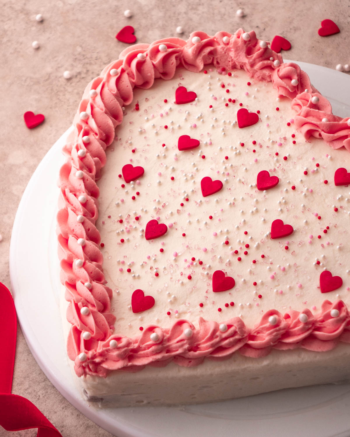 corner of a heart shaped cake decorated with pink icing and heart sprinkles