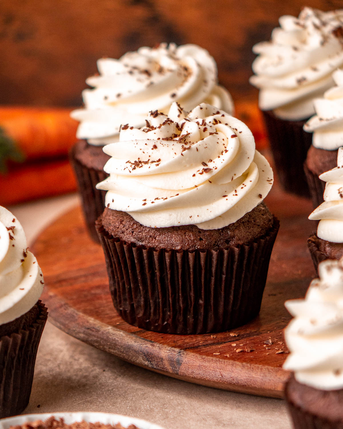 chocolate carrot cake cupcakes on a wood tray with carrots in background