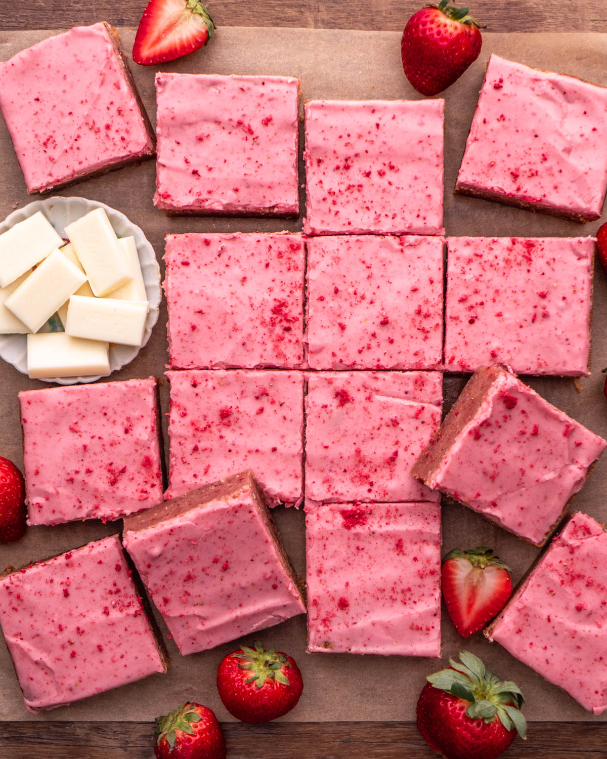strawberry brownies arranged on parchment paper with strawberries and white chocolate around 