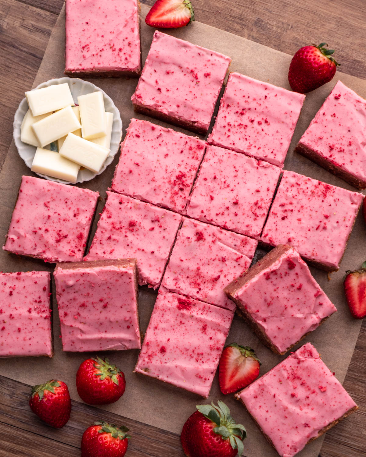 strawberry brownies arranged on parchment paper with strawberries and white chocolate around