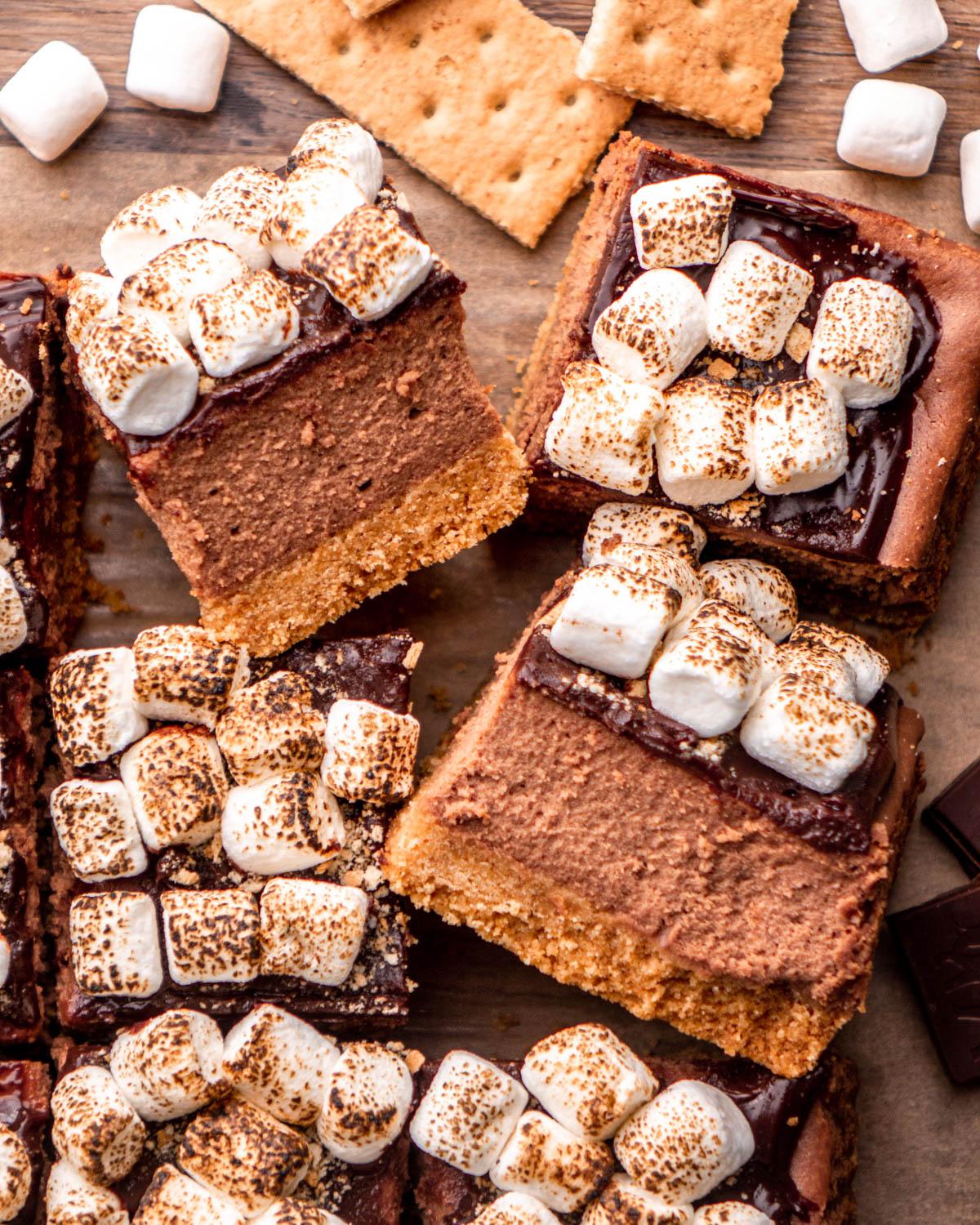 close up of cut s'mores cheesecake bars arranged on parchment paper with marshmallows, graham crackers and chocolate around